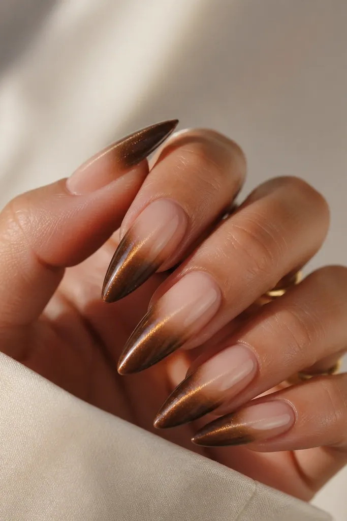 Long almond nails where the cuticle area is sheer nude and fades into warm umber cat eye toward the tip. The cat-eye stripe stays centered across the fade.