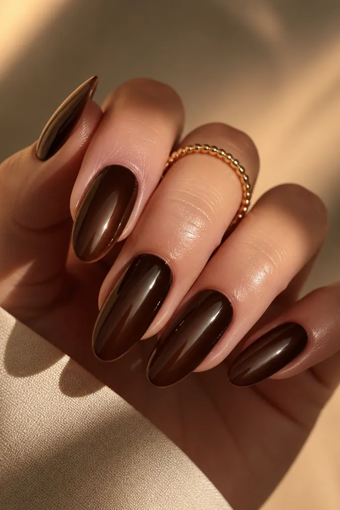 Long almond nails in deep espresso brown cat-eye polish with a single bright vertical stripe from cuticle to tip; glossy black-brown shine in the background.