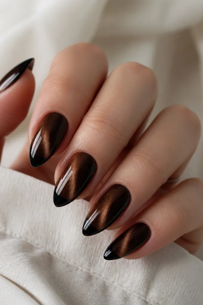 Medium almond nails with dark brown cat-eye on most of the nail and a glossy black patent-like tip; the stripe continues through the brown area only.