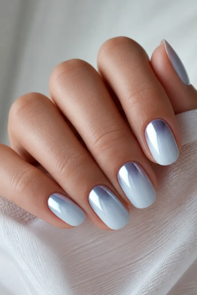 Short oval nails with a milky white-to-ice-blue ombre from cuticle to tip; the top third is mirror chrome in pale icy blue, reflecting light like glass.
