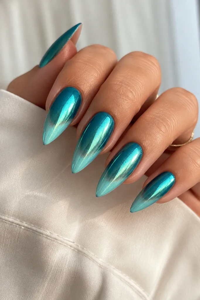 Medium stiletto nails with teal fading from cuticle to a lighter turquoise tip; blue-green chrome powder shifts color under light.