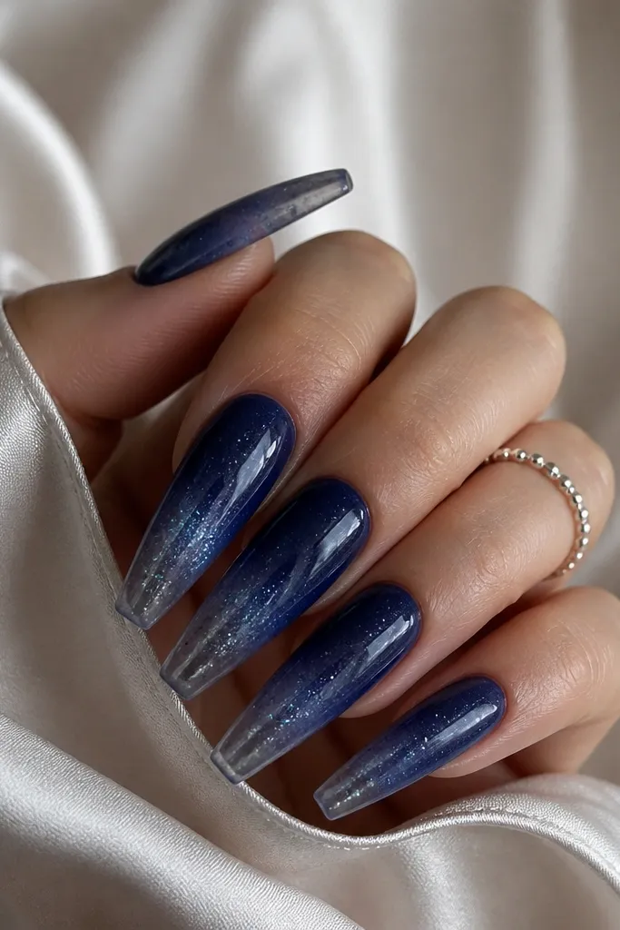 Long coffin nails with deep blue ombre fading into smoky clear; speckled galaxy chrome spray adds tiny silver-blue dots across the surface.