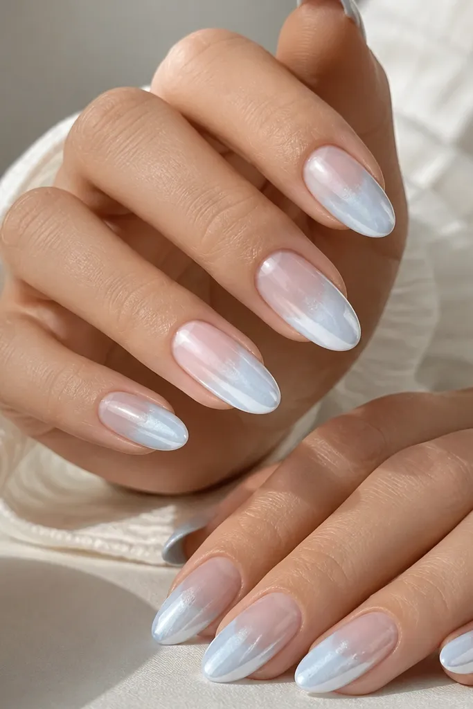 Medium almond nails with light blue fading to clear; white chrome is applied in a soft cloud patch across the center and tip, leaving cuticle mostly sheer.