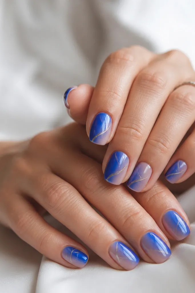 Short squoval nails with royal blue ombre fading to sheer; two to three thin chrome silver lines run diagonally from the side of the nail toward the center.