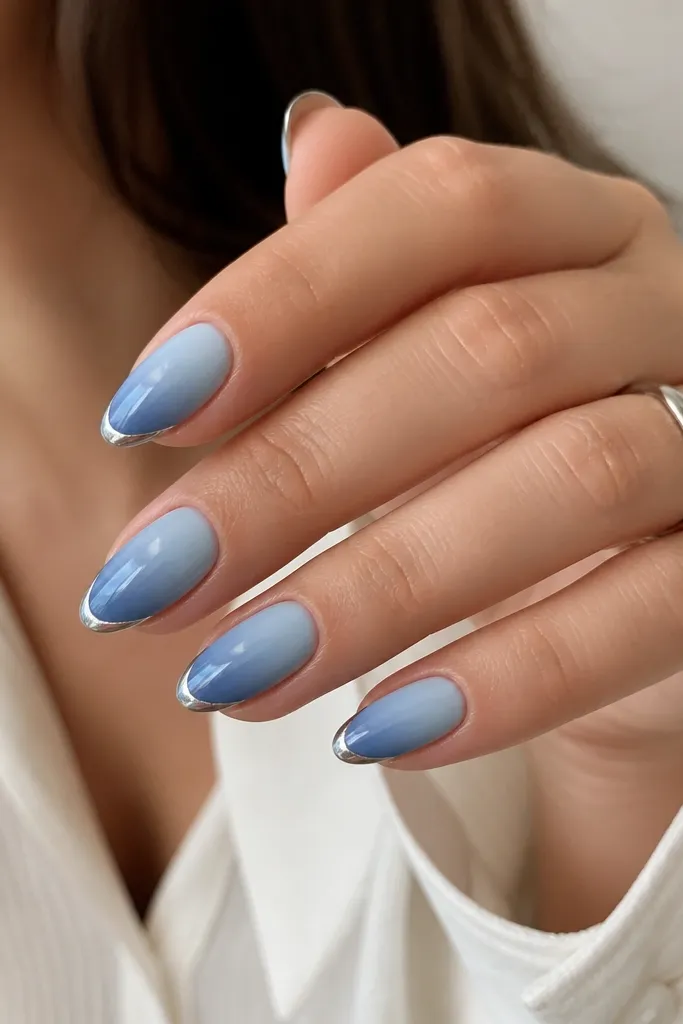 Medium almond nails with blue ombre from cuticle to tip; a reverse French arc in chrome outlines the tip border like a crescent frame.