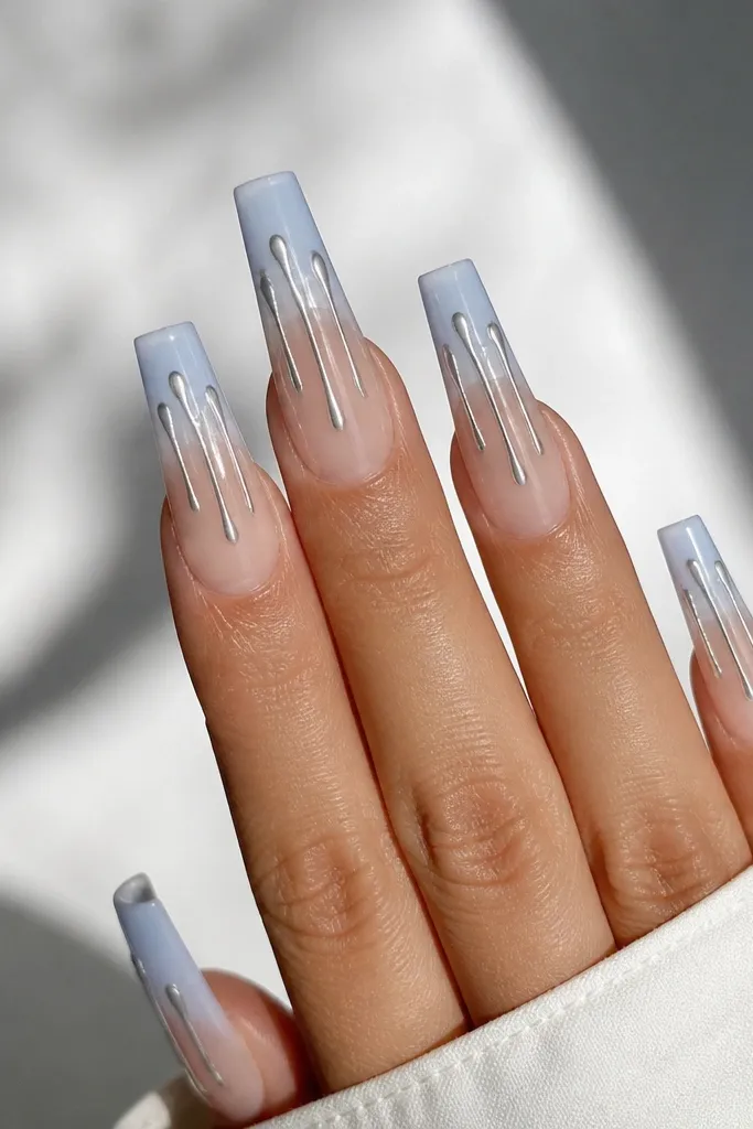 Long coffin nails with powder blue ombre fading to sheer; thin silver chrome drip shapes hang from the tip area toward the middle.