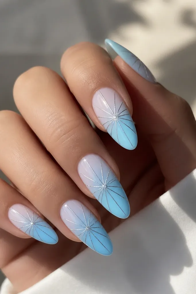 Long almond nails with sky blue ombre; chrome silver lines radiate from the center like a tiny starburst.