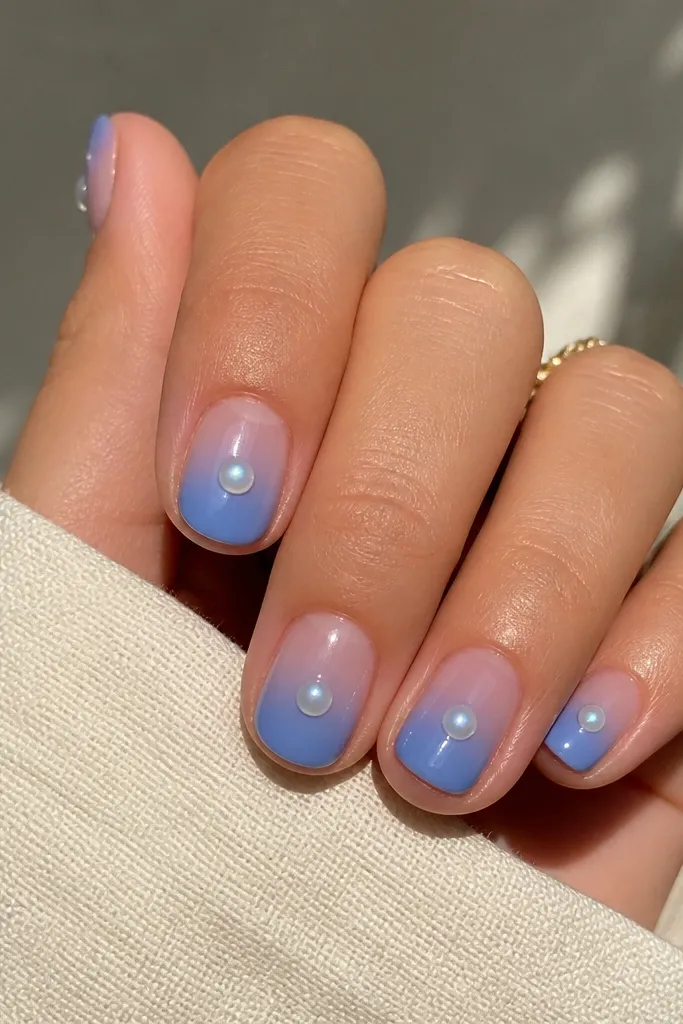 Short rounded nails with blue ombre; a single pearl chrome dot sits in the center of each nail like a tiny gem.
