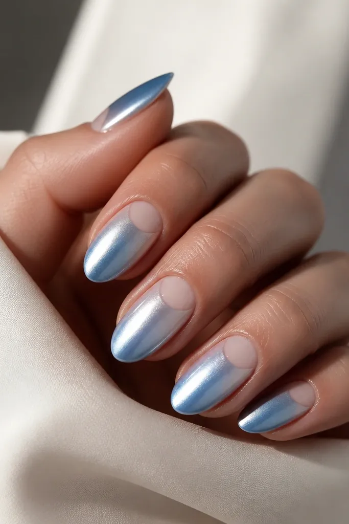 Medium almond nails with silver-blue ombre; a negative space half-moon near the cuticle is left clear, then chrome is applied on the rest.