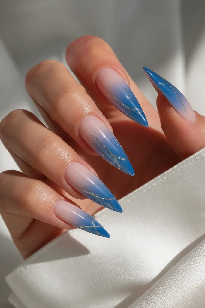 Long stiletto nails with blue ombre; thin chrome veins in silver run diagonally like marble, crossing the gradient.