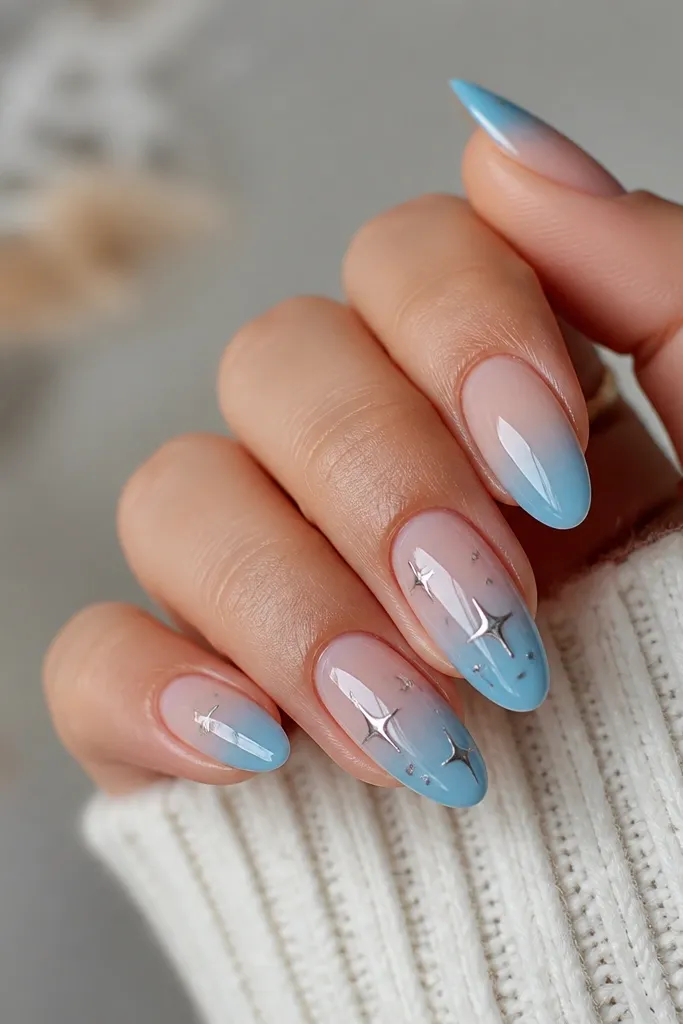Medium oval nails with deep blue tips fading to sheer; on two accent nails, small star shapes in silver chrome sit inside a thin halo ring near the center.