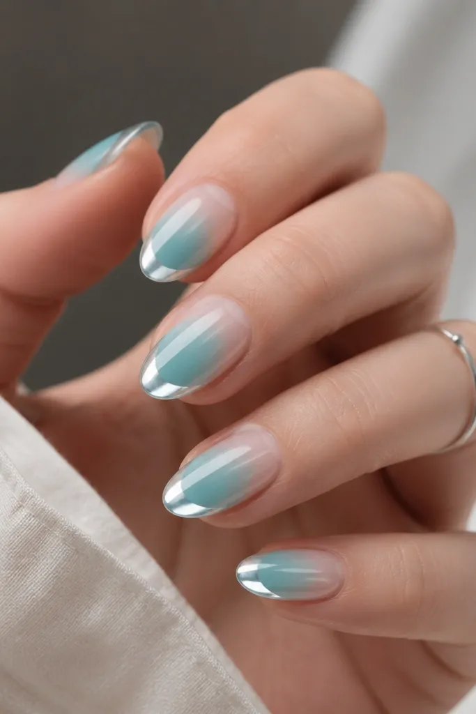 Short almond nails with cyan ombre fading to milky clear; mirror chrome is applied as a glossy "lip" band across the very tips.