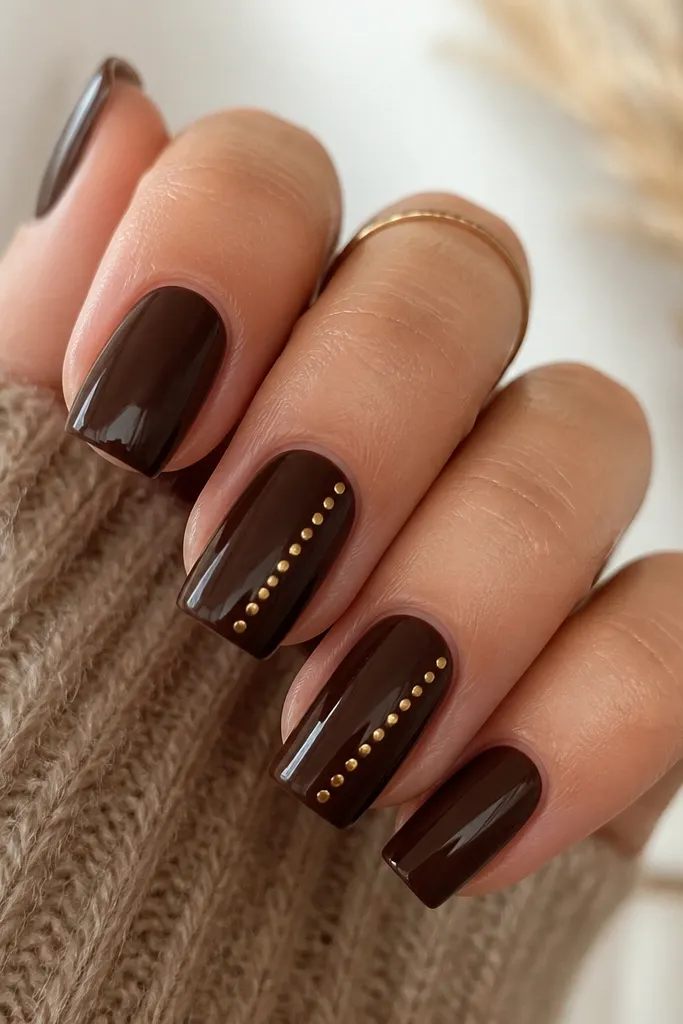 Square nails in deep espresso brown. On two accent nails, small gold polka dots appear along one diagonal line; the other nails have plain brown with glossy shine.