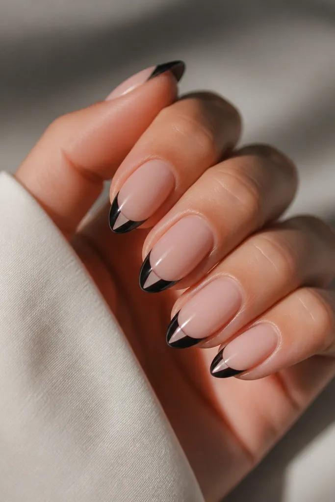 Short stiletto nails with a glossy nude base; a black French line wraps the tip; in the center of each nail near the tip, a clear triangle negative space area remains unpainted.