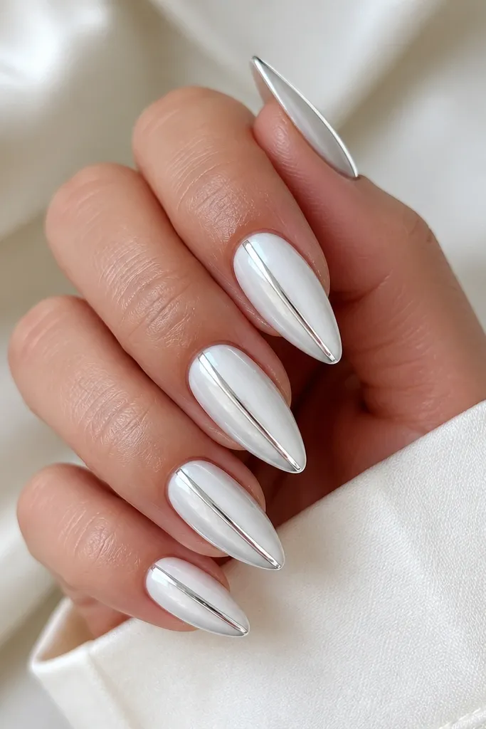 Short stiletto nails with an icy white opaque base; on each nail a vertical silver chrome stripe runs along one side from near the cuticle to the tip; glossy top coat.