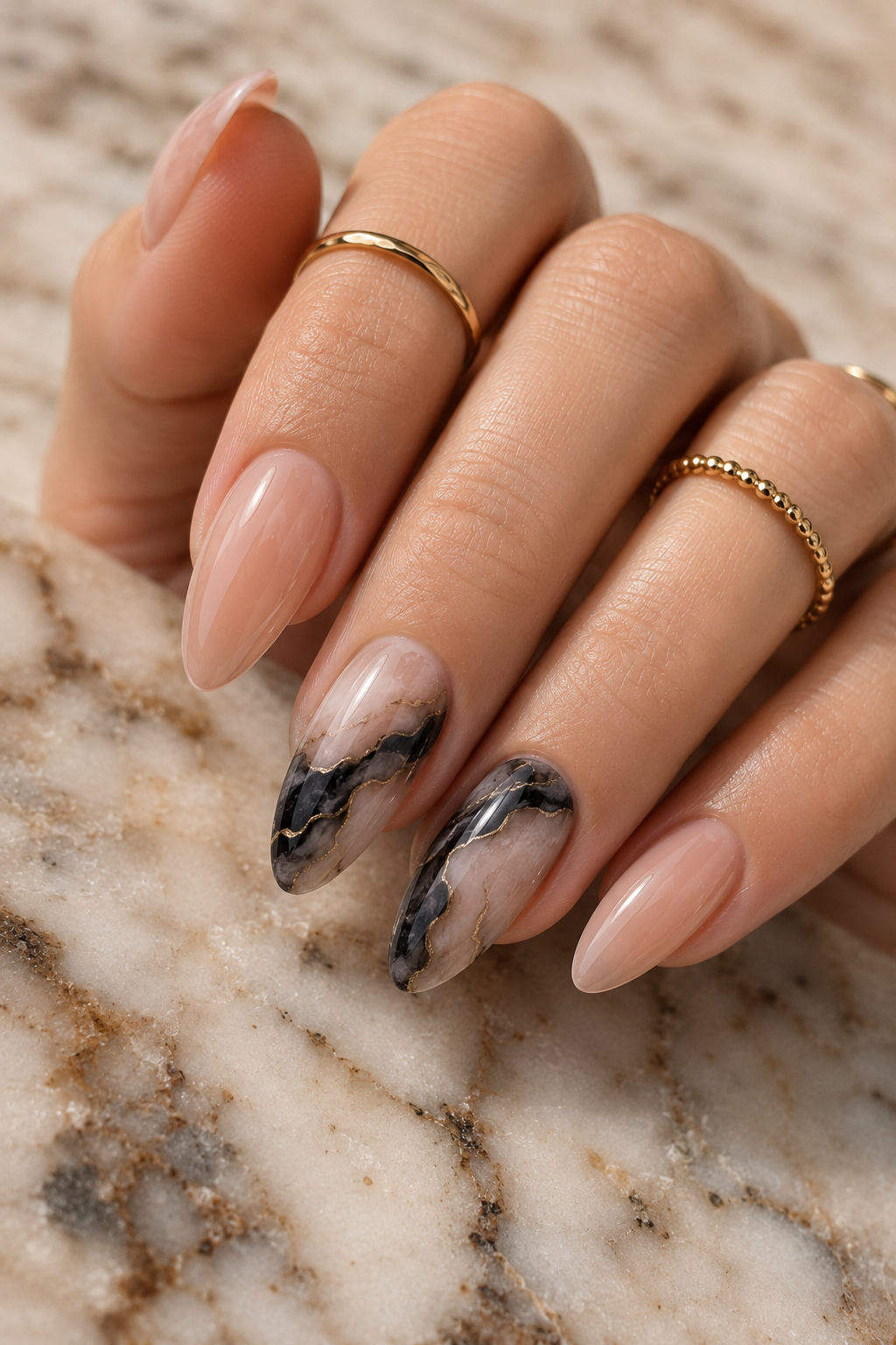 Short stiletto nails mostly nude pink glossy; two accent nails have black marble veining with thin white lines over a milky nude base; marble looks airy and not chunky.