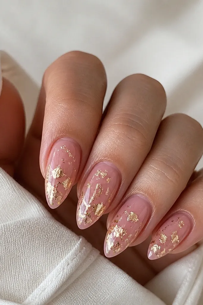 Short stiletto nails with a clear pink jelly base; gold foil flakes are scattered mostly near the center and lower half; some flakes look torn and irregular; glossy top coat.