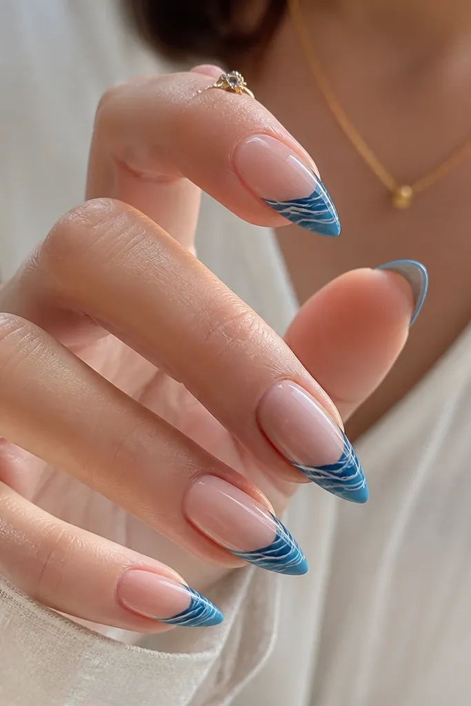 Short stiletto nails with nude base; tips are painted ocean blue; on top of the blue tips are thin white wave lines running horizontally; glossy finish.
