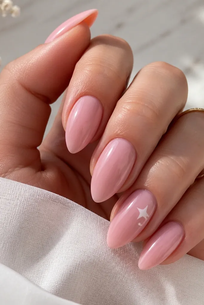 Short stiletto nails in soft pink glossy; on one accent nail there is a small white five-point star near the cuticle and a tiny dot beside it; other nails are plain.