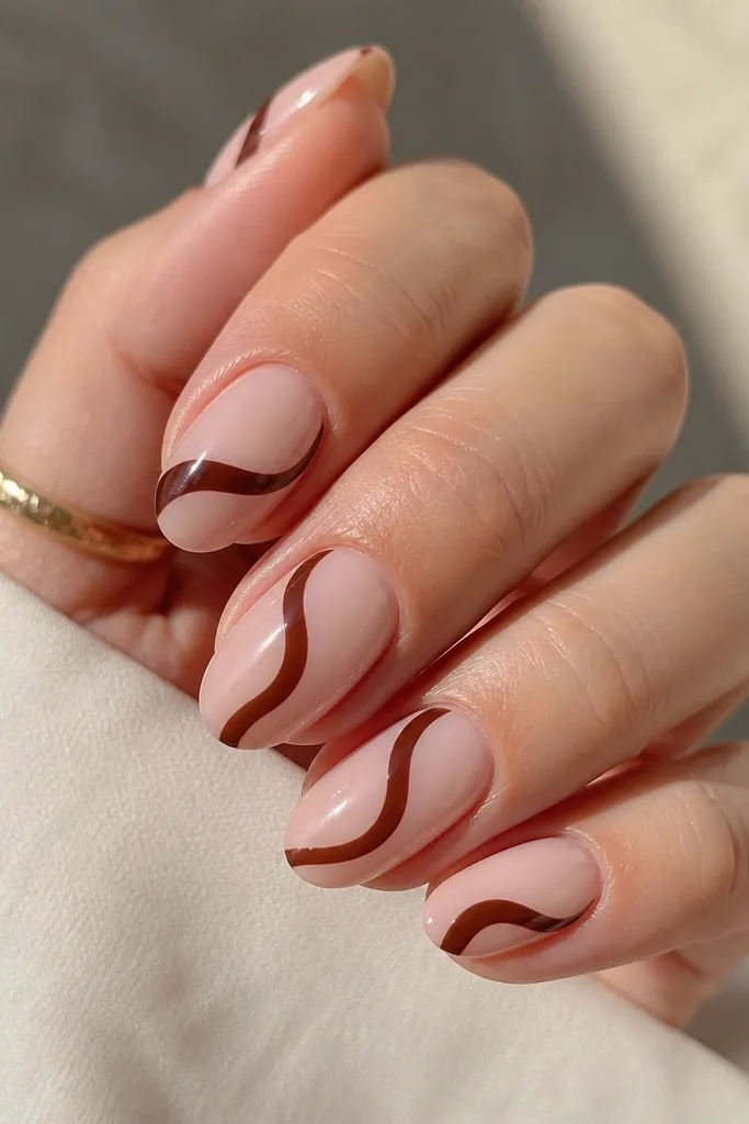 Medium oval nails with a nude base. One curved espresso swirl sits on each nail, leaving a large nude area inside the swirl. Glossy finish.