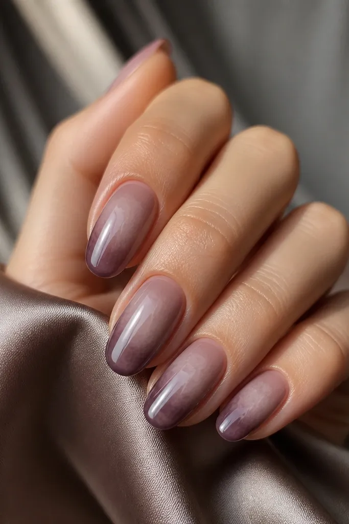 Oval nails with a smoky mauve gradient. The tips are deeper mauve and the center has a cloudy, airbrushed look. Chrome is applied lightly so it fades out toward the cuticle, leaving the base semi-matte compared to the shine at the tip.