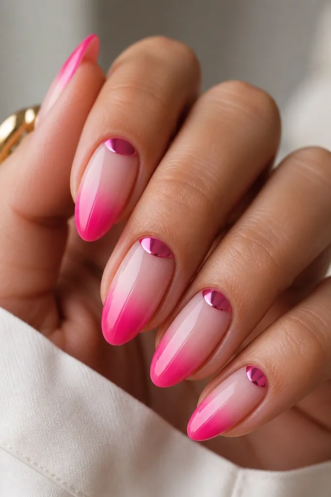 Medium almond nails. The ombre fades from sheer blush at the cuticle to hot pink at the tip. A half-moon chrome shape sits near the cuticle area in hot pink chrome, leaving the rest of the nail ombréd and glossy.