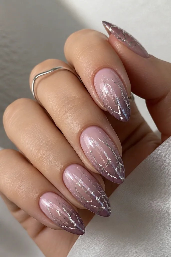 Almond nails with dusty mauve tips fading into a soft mauve-pink near the cuticle. Chrome is applied in a cracked-ice pattern with broken reflective lines, especially around the center and edges.