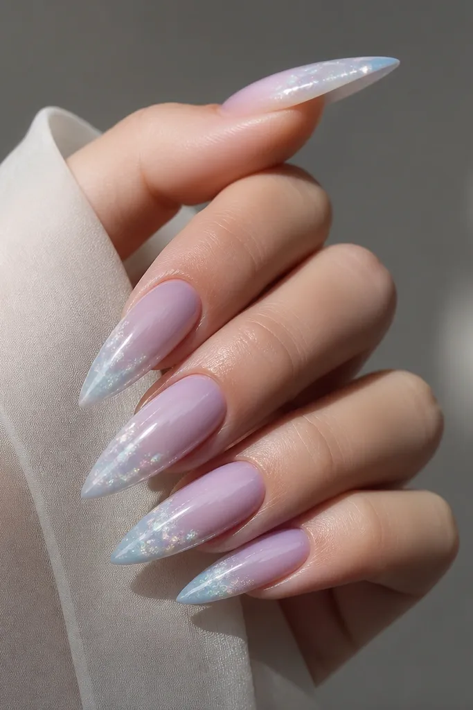 Stiletto nails with a lilac-to-ice blue ombre that looks smoky in the tip area, with chrome dust concentrated in a cloudy band near the free edge.