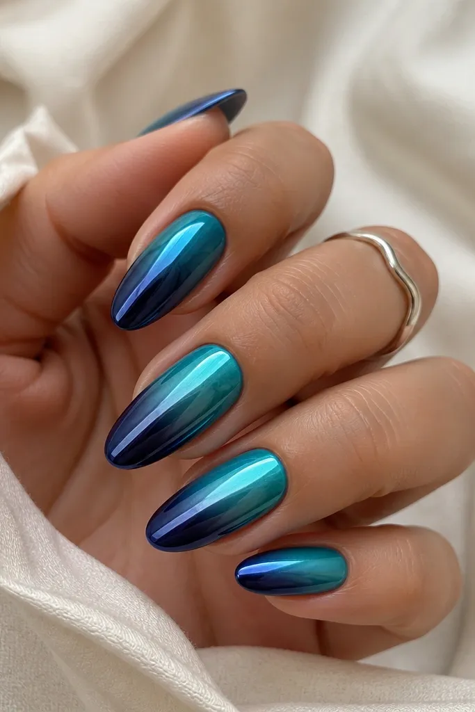Medium almond nails fading from ocean teal at the cuticle to deep navy at the tip, with a vertical mirror chrome stripe running down the center.