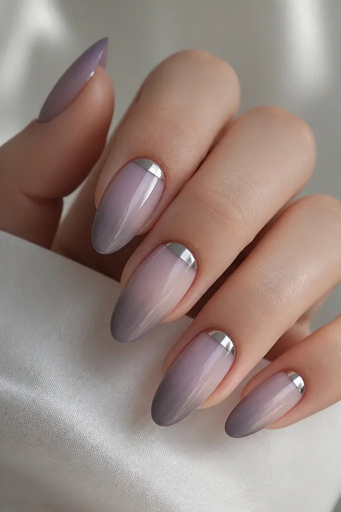 Almond nails fading from sheer lavender at the cuticle into smoky gray-lilac at the tips, with a chrome half-moon near the cuticle.