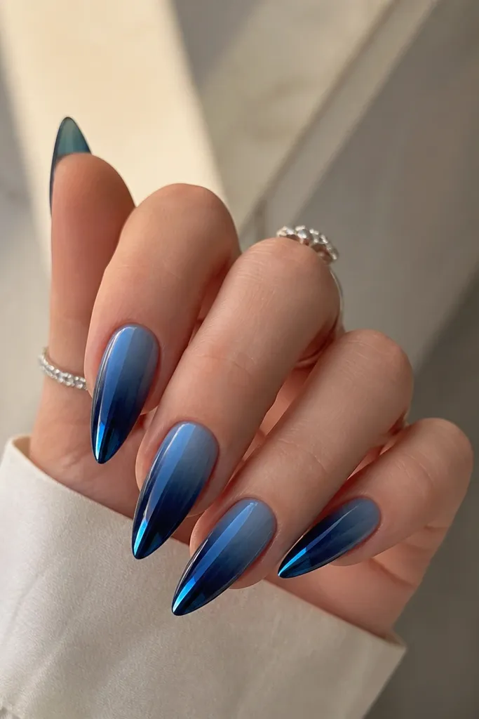Long almond nails with deep navy at the tips fading into a lighter denim blue near the cuticle, finished with blue mirror chrome at the very end.