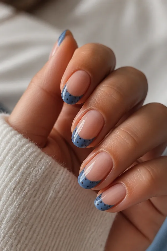 French-tip style: the tips are painted denim blue with a clean curved line. Each nail has 5-8 tiny chocolate-brown dots sprinkled across the blue tip area.
