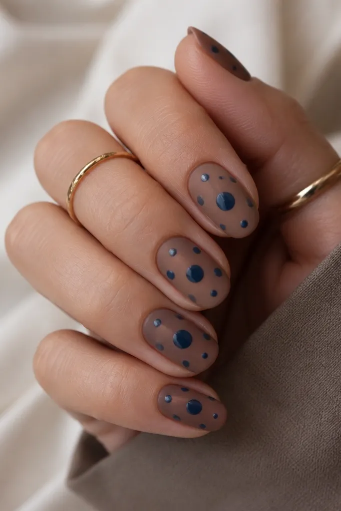 All nails are matte taupe-brown. Each nail has glossy navy polka dots scattered in a loose pattern, with the largest dot near the center.