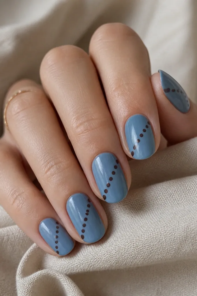 All nails have a medium denim-blue base. A diagonal line runs from lower left to upper right with a series of chocolate-brown dots placed along it.