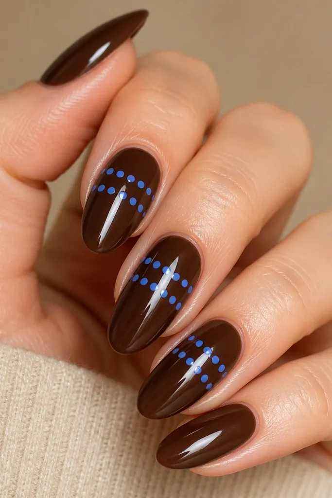 All nails are glossy brown. Each nail has two straight rows of navy dots: one row across the middle and one row closer to the tip.