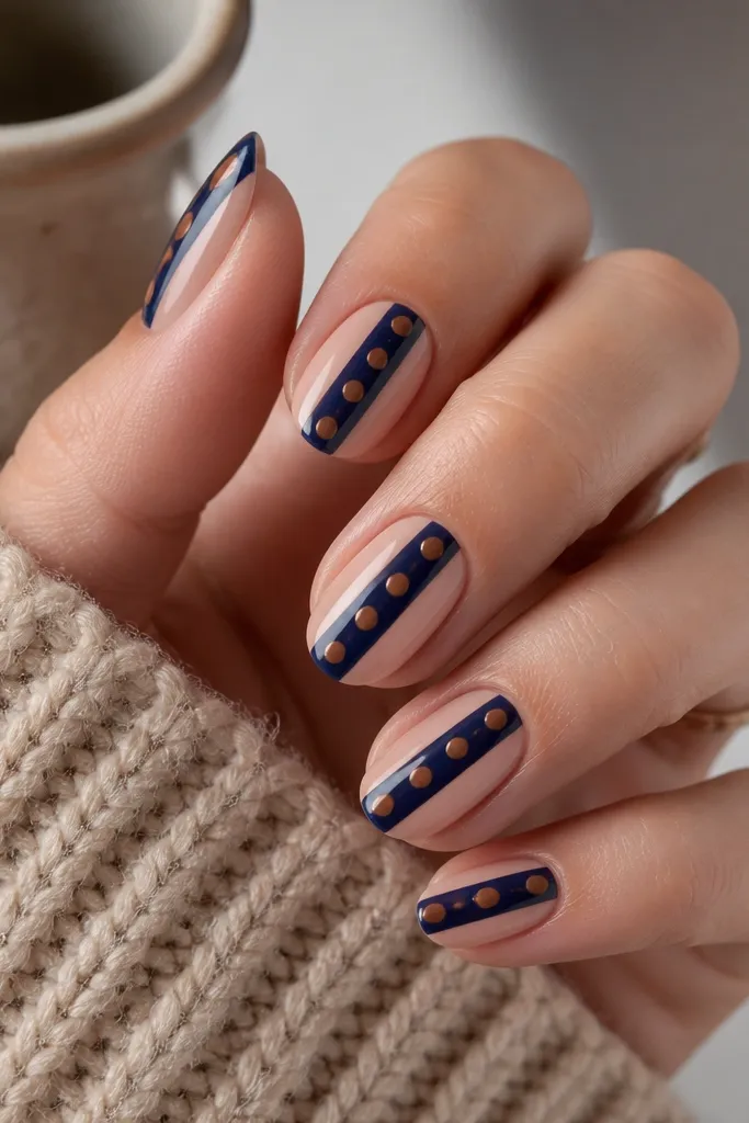 Nails have a nude base with a single glossy navy stripe running vertically down the center. Over the stripe are brown polka dots spaced evenly.