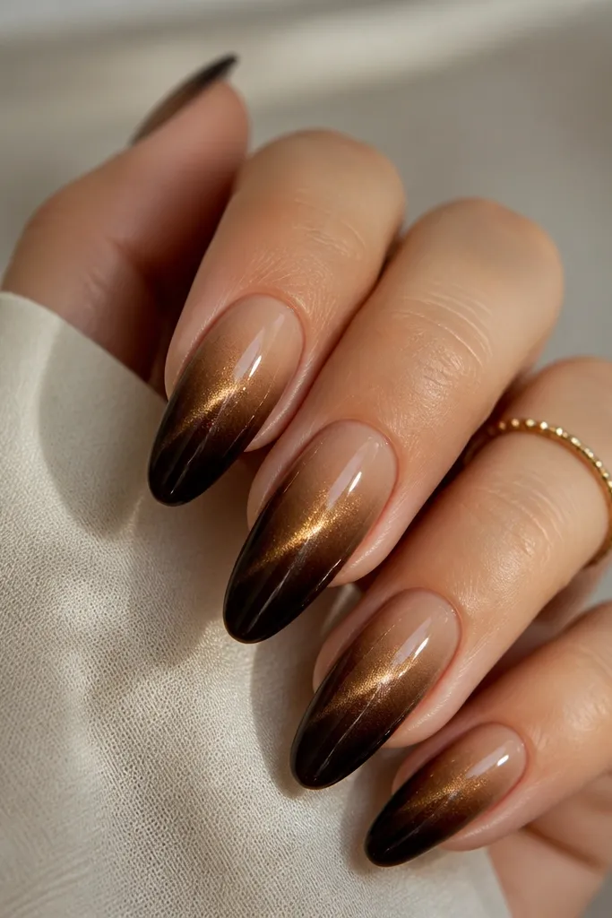 Ombre nails that start nude-beige near the cuticle and fade into espresso brown. A gold cat-eye streak runs through the darker half, strongest at mid-nail. Glossy top coat.