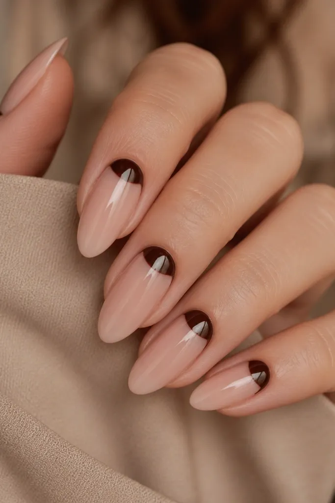 Almond nails with a deep espresso-brown half-moon at the cuticle, leaving the rest of the nail bare nude; the half-moon shape is sharp and centered.