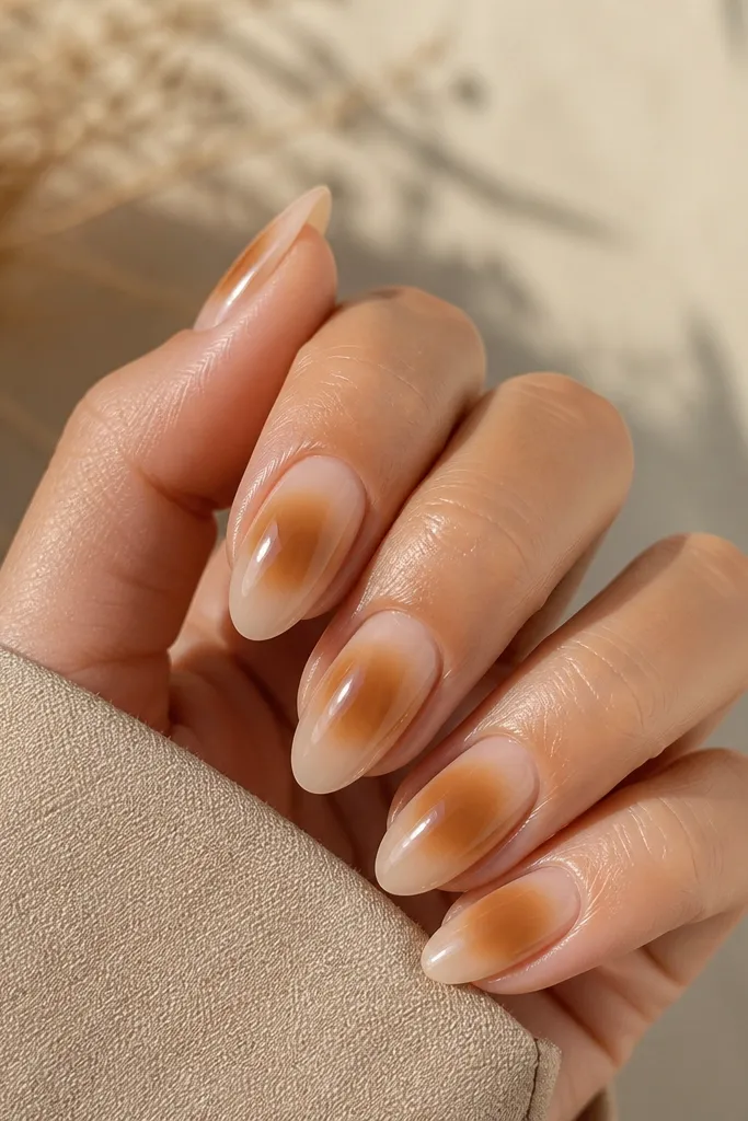 Medium almond nails with a nude base and a soft toffee-brown aura around the center of the nail, blending outward with no hard edges.