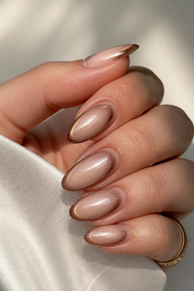 Almond nails with a nude base, each nail has a thin halo ring of brown chrome around the center, with a glossy topcoat that makes it glow.