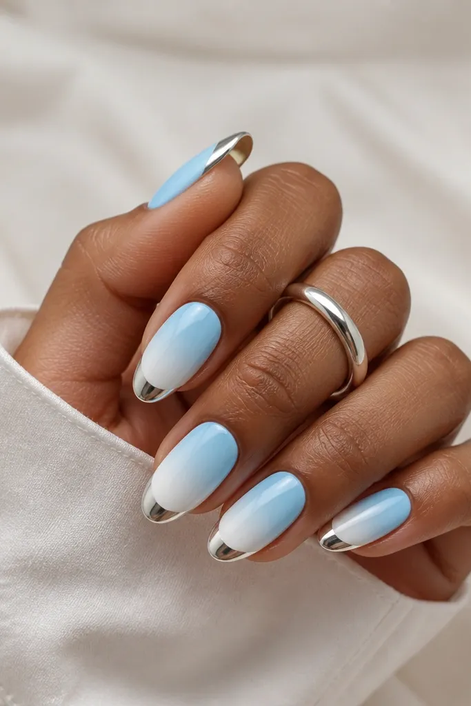 Medium almond nails with a sky-blue fade that lightens into white at the tip; a bright silver chrome cap sits right on the white tip area.