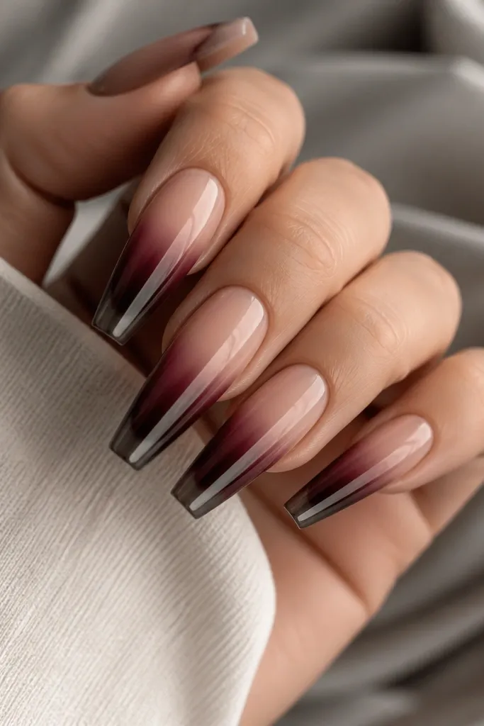 Long coffin nails with nude beige near the cuticle fading into deep burgundy tips; the tips are coated in blackened chrome for a smoky mirror effect.