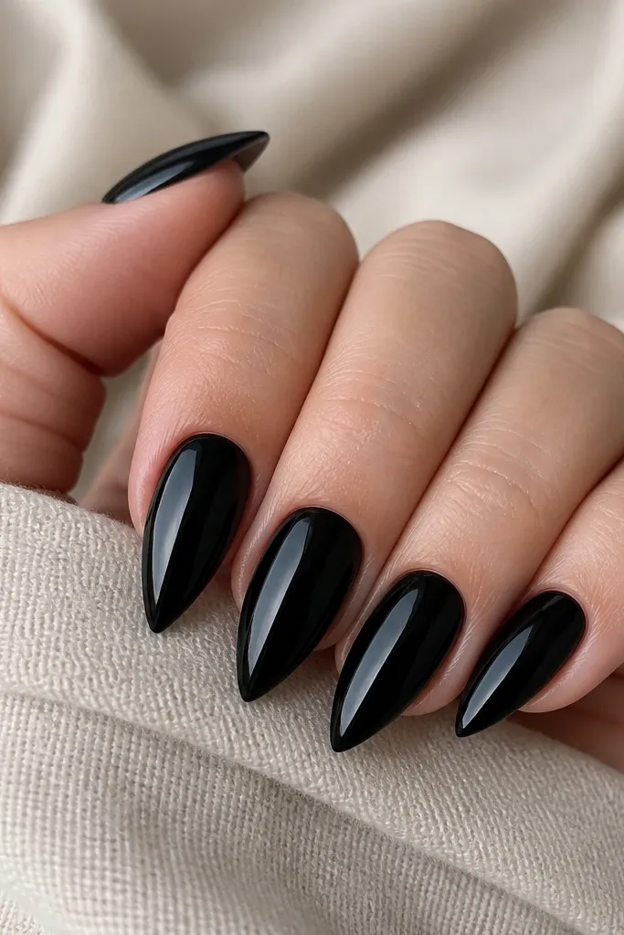 A full set of 10 short stiletto nails in solid true black with a high-gloss shine; tips are narrow and pointed, and the cuticle lines look crisp and even.