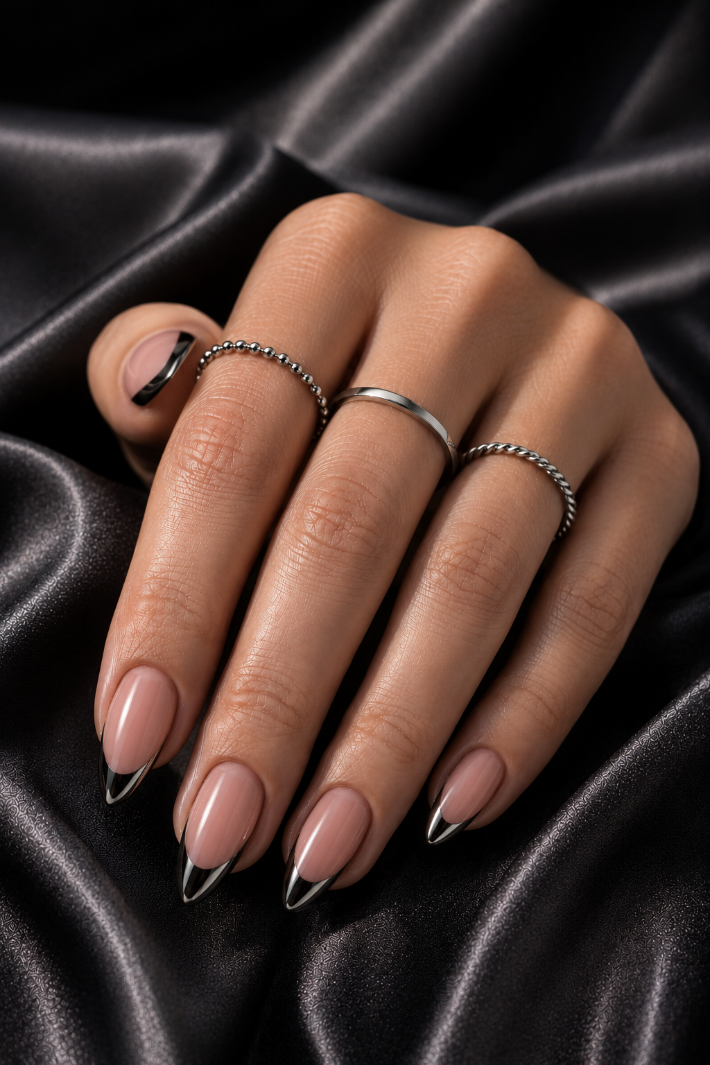 Short stiletto nails with solid black bases; the tips have a reflective chrome band like a curved half-moon, transitioning from black to silver-black shine.