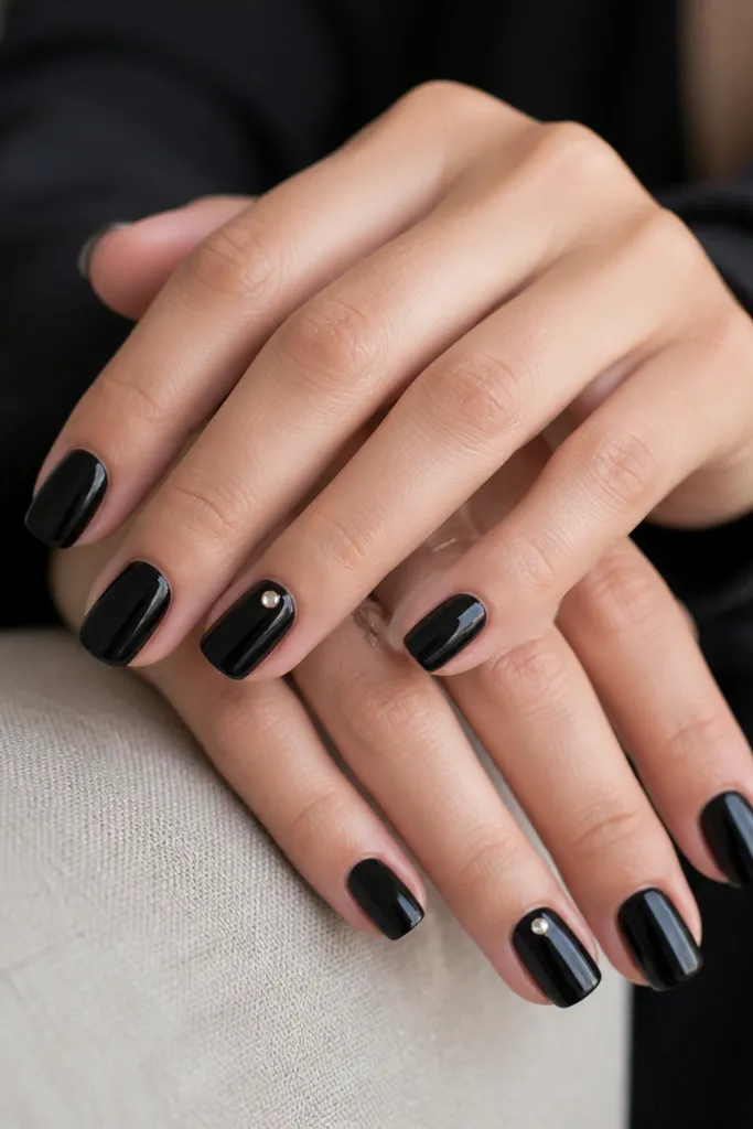 Mostly solid black nails; two accent nails have one small silver stud near the upper third of the nail with a glossy finish.