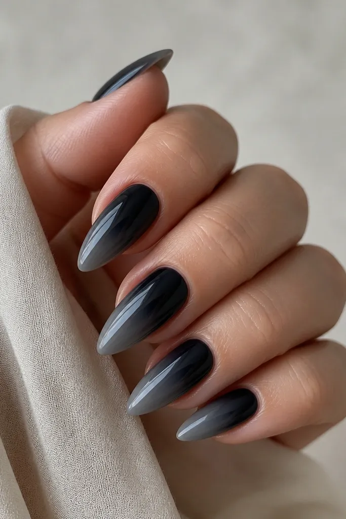 Short stiletto nails with black at the base fading into smoke gray toward the tip, with a glossy finish and smooth edges.