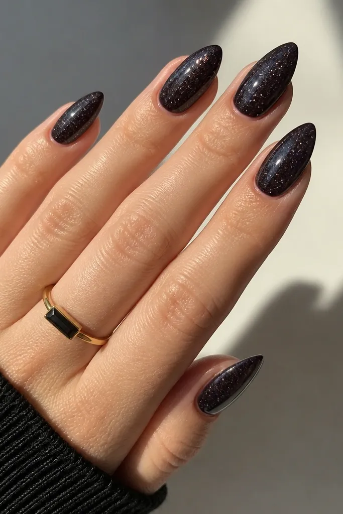 Short stiletto nails with a dark jelly-black look; the top coat has visible glitter suspended throughout, giving a translucent sparkle.