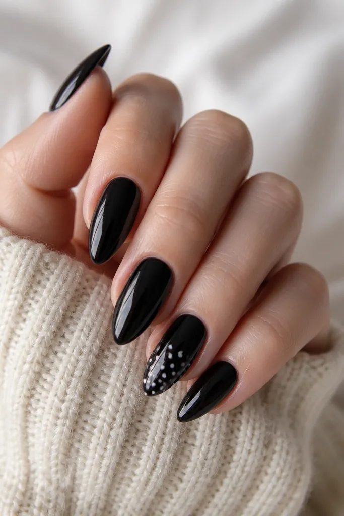 Mostly solid black short stiletto nails; one accent nail has tiny white polka dots scattered evenly near the tip, with glossy shine.