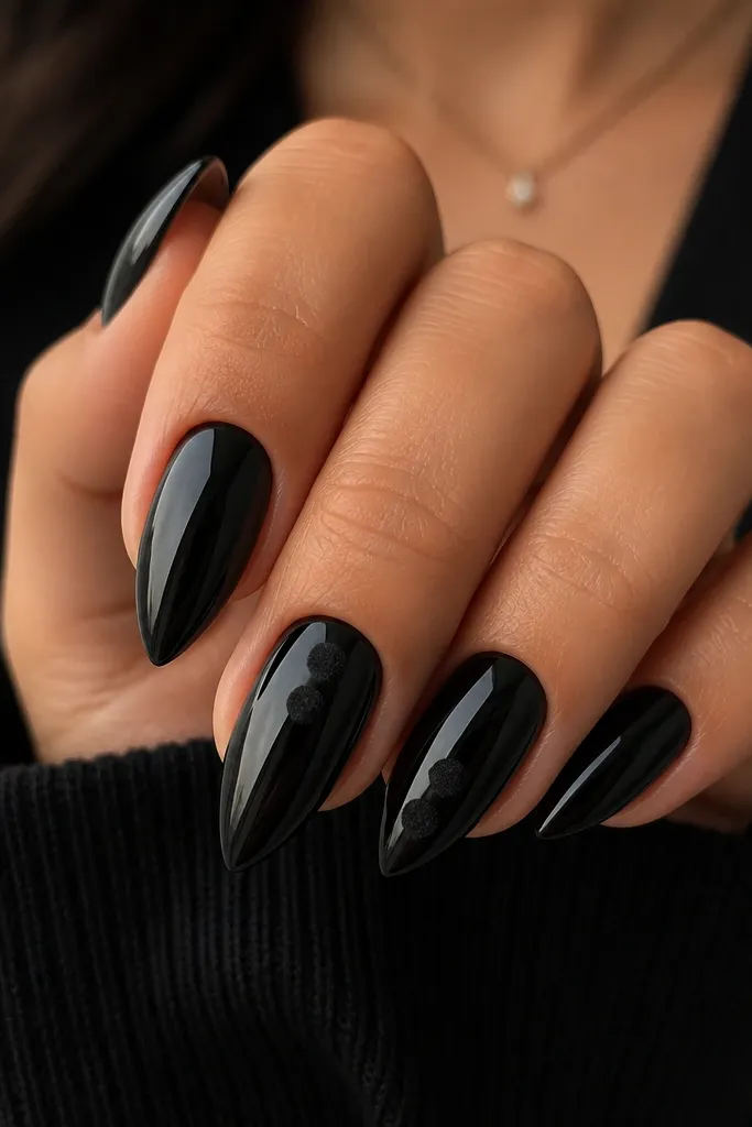 Short stiletto nails with glossy black base; small matte, velvety black dots appear on two accent nails near the center and tip.
