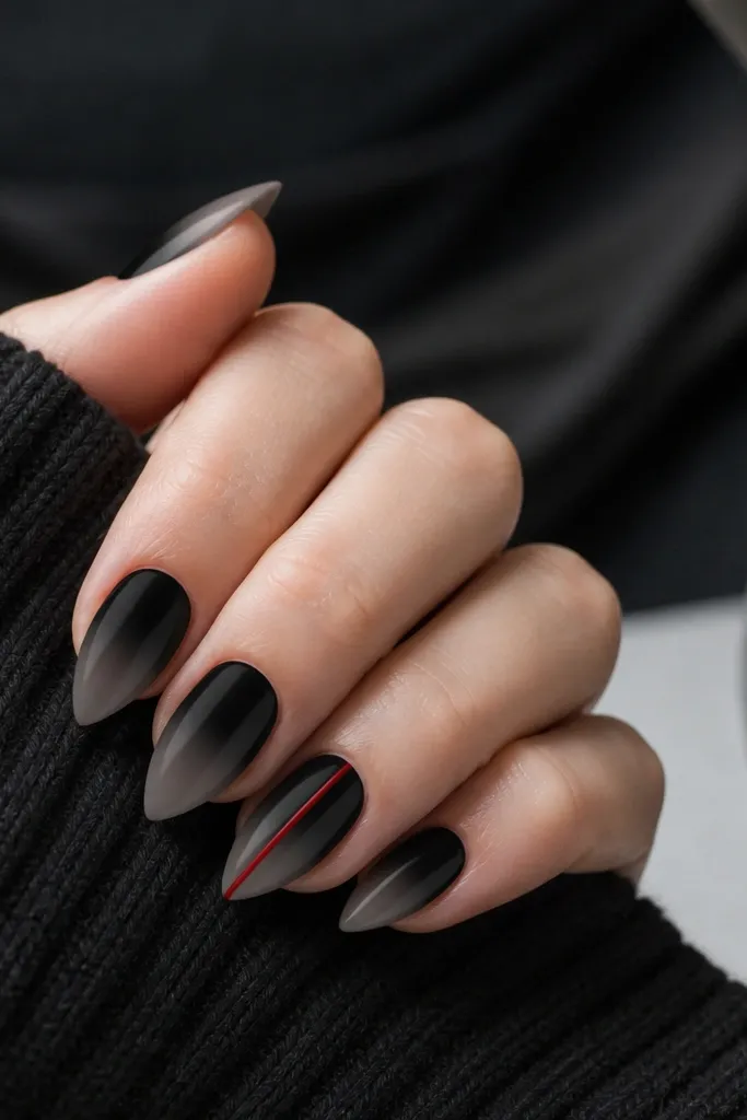 Short stiletto nails with black fading slightly lighter toward the tip; one accent nail has a single thin red line running vertically down the center.